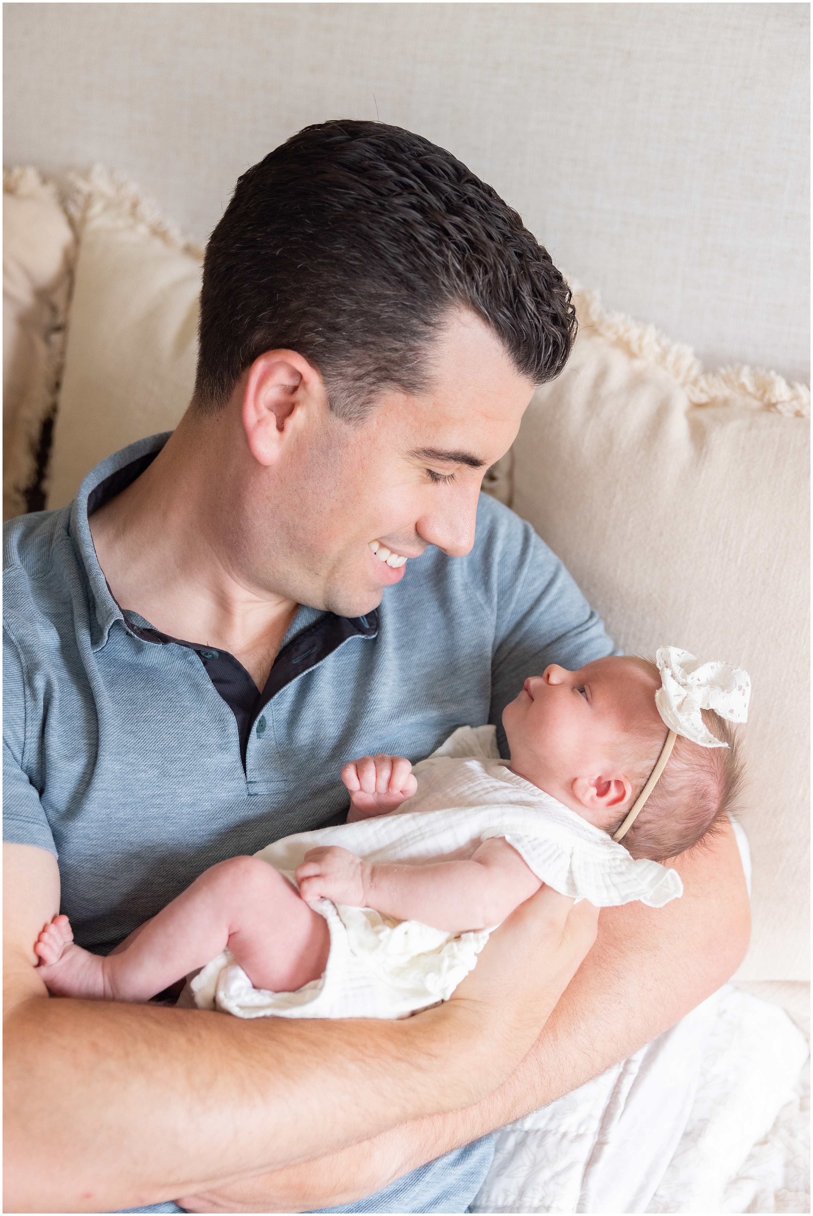 A dad smiles as he cradles his baby girl, gazing at her warmly in a soft, cozy home setting.