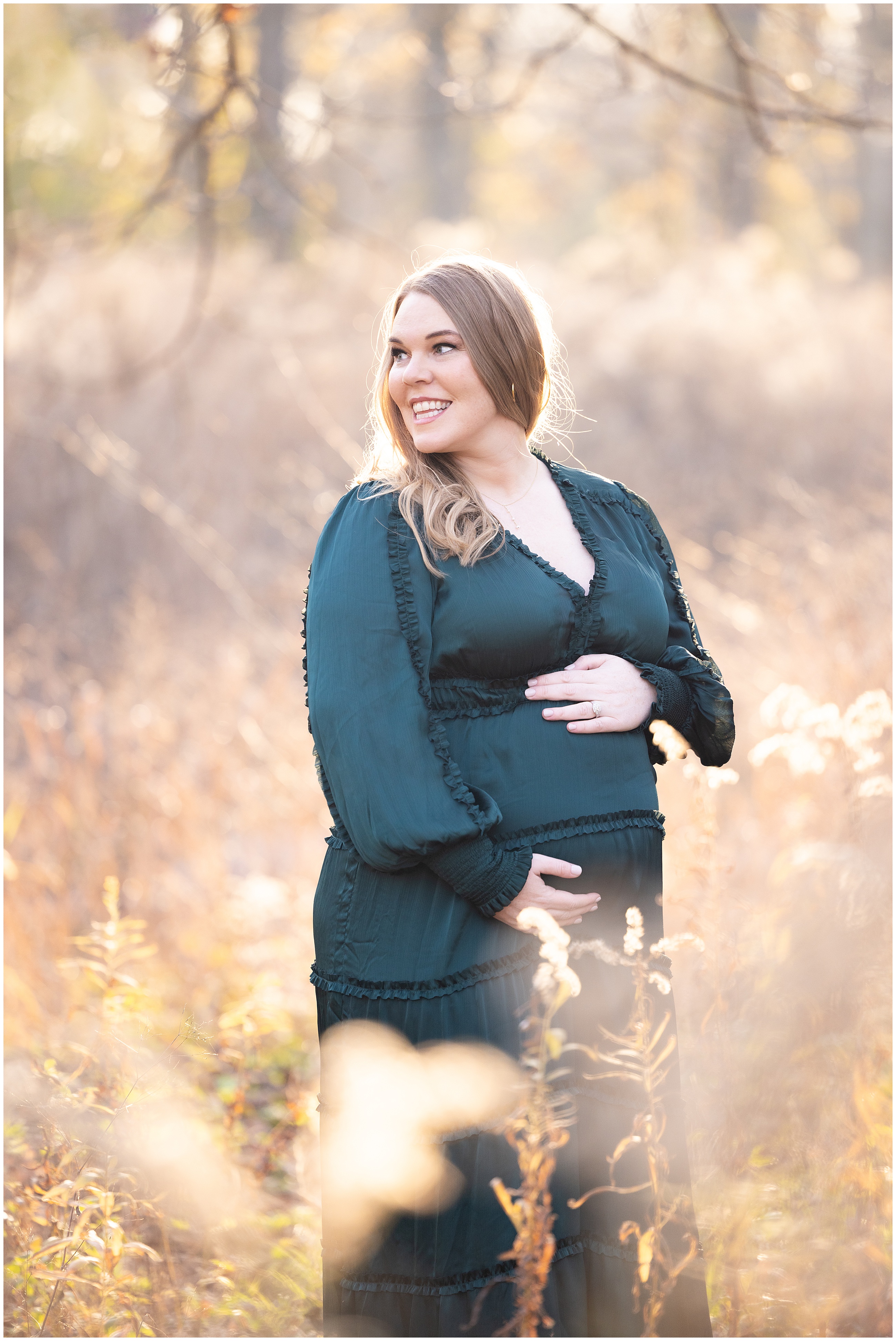 Pregnant woman in green dress smiling, holding her belly in a sunlit meadow. Soft, warm light creates a serene and joyful mood.
Columbus, Ohio maternity photo.
