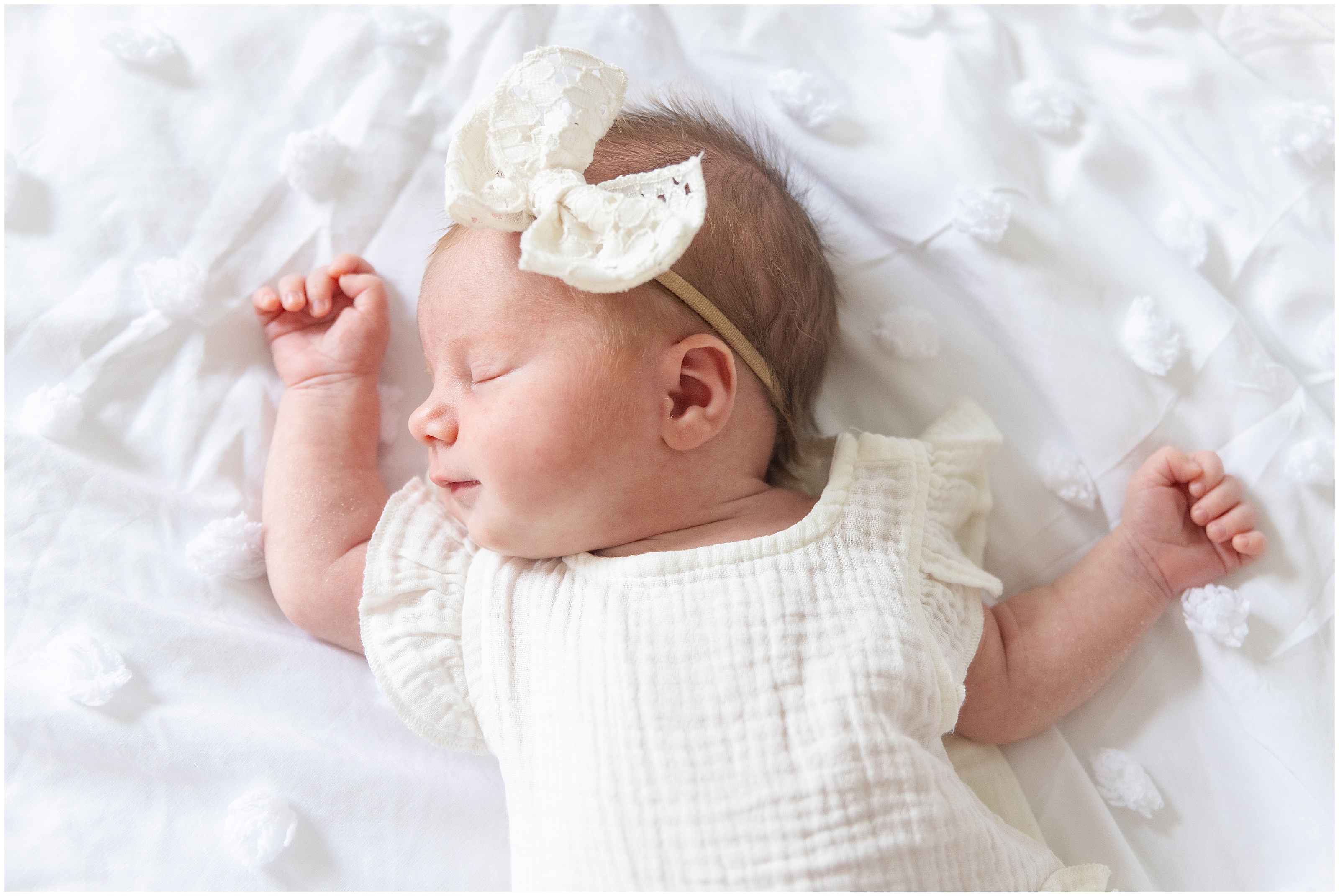Sleeping newborn baby girl in a white dress and bow headband on a white quilt, peaceful and serene with soft natural light